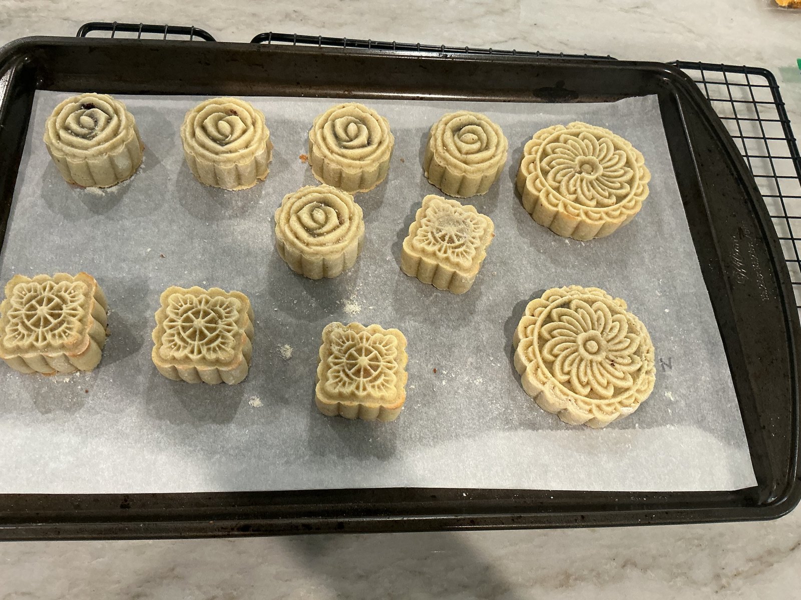 Unbaked mooncakes with rose, flower, and square patterns on a lined tray