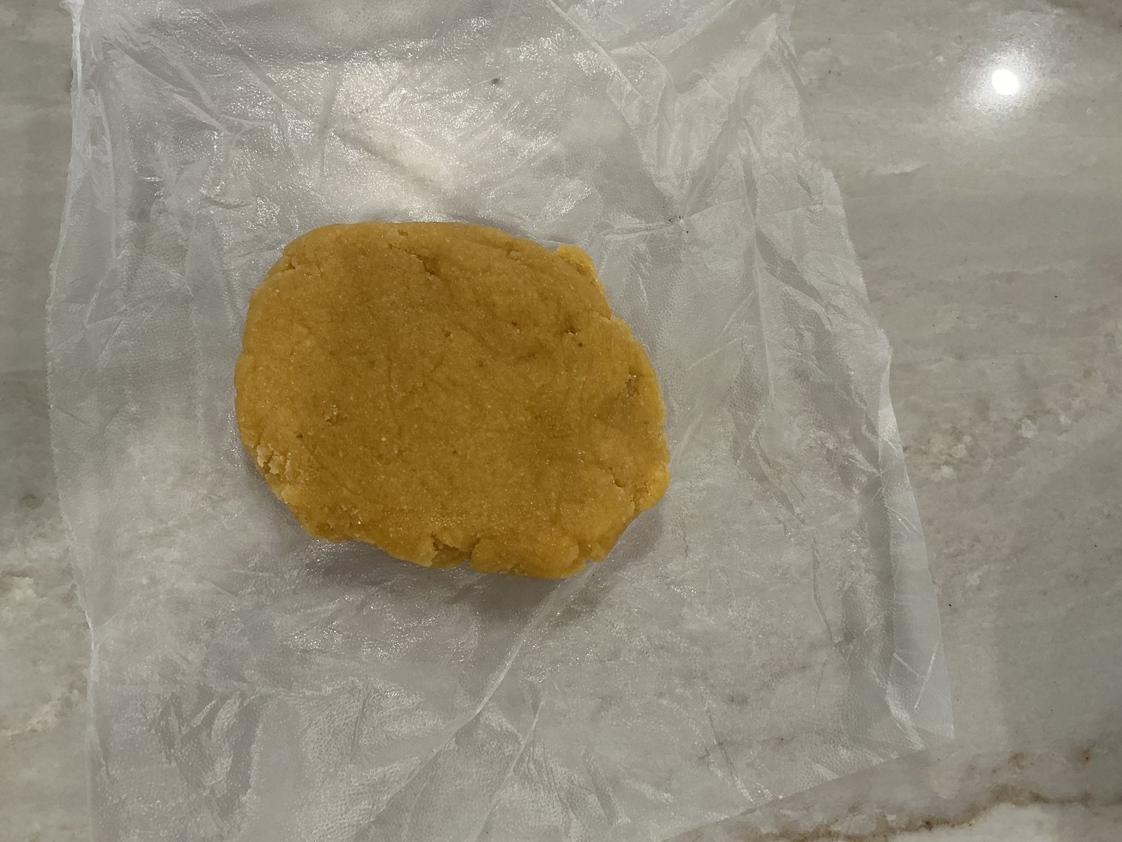 A soft yellow dough disk resting on plastic wrap