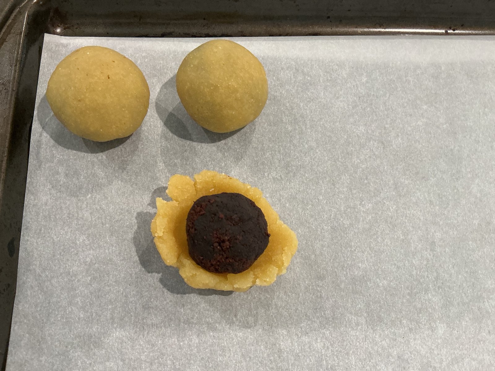 A dark brownie ball centered in a flattened dough wrapper beside two enclosed dough balls